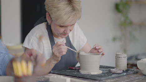 Woman-Potter-Attaching-Handle-To-Mug-In-Ceramics-Studio.-Female-potter-shaping-and-carving-mug-in-pottery-workshop-studio